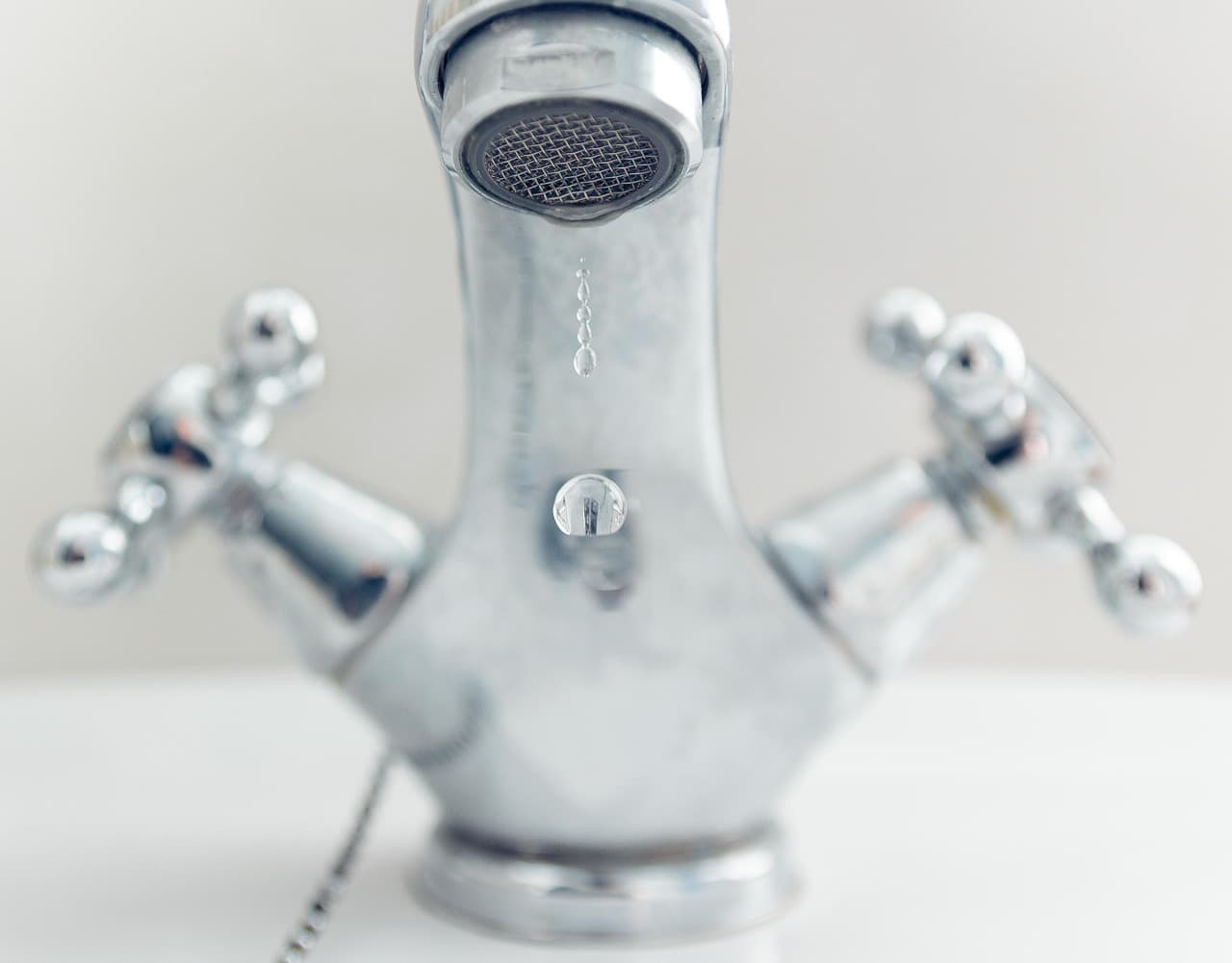 A chrome basin mixer with cross-head handles, a drop forming at the spout