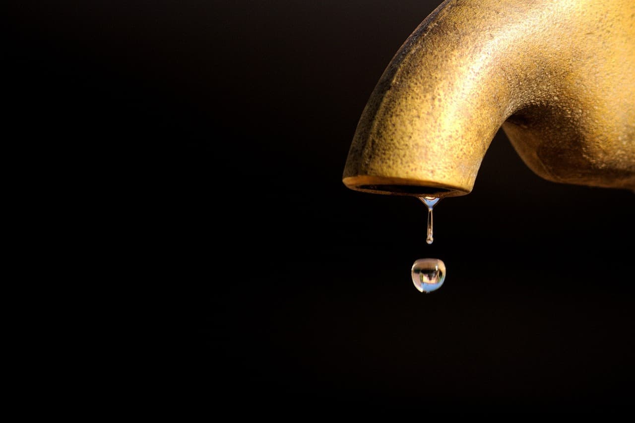 A single drop falling from a brass tap