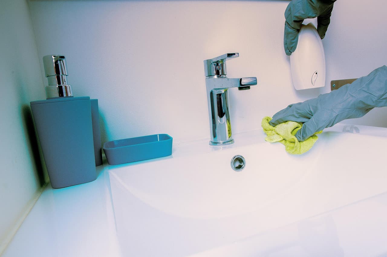 A gloved hand wiping down a white basin and its chrome tap